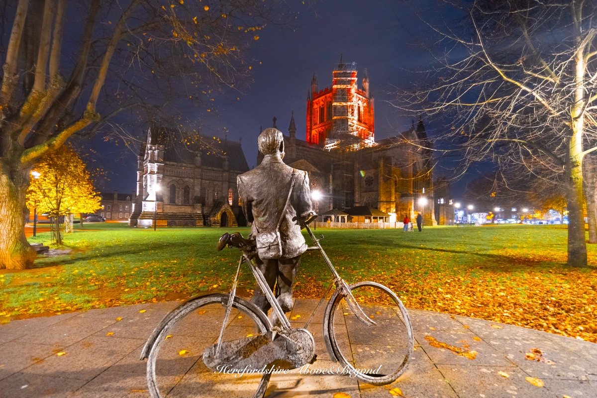 Statue of a cyclist in front of Hereford Cathedral at dusk in autumn
