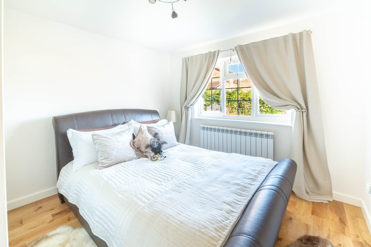 Bedroom with a leather sleigh bed, white bedding and cream curtains