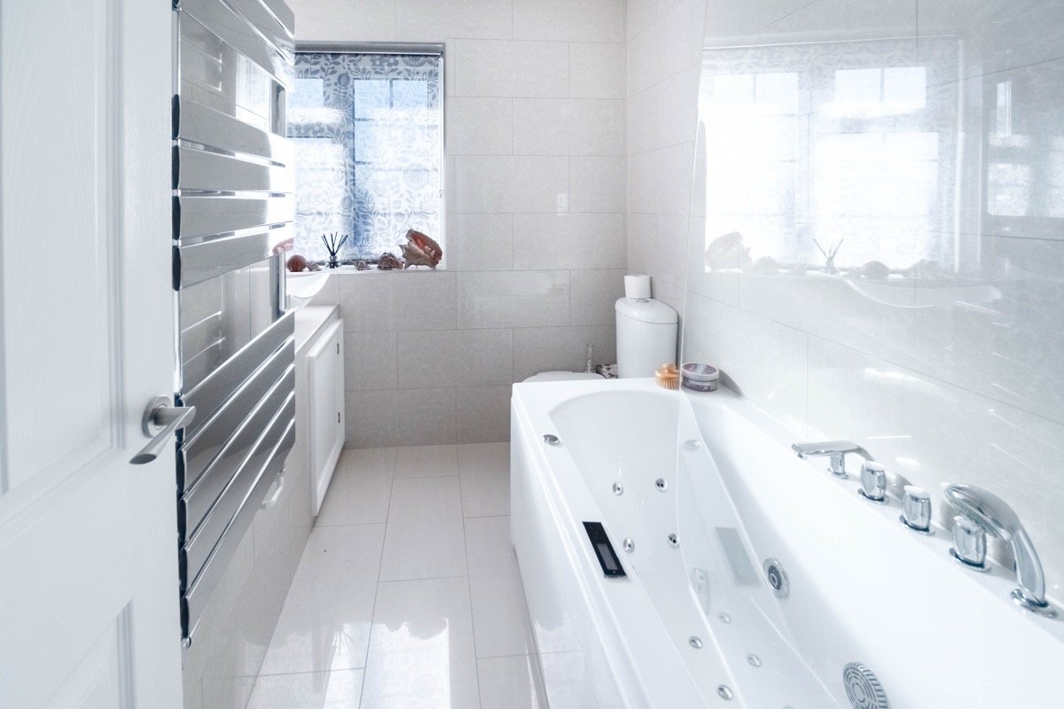 Bathroom with a whirlpool bath, chrome towel radiator and large white tiles