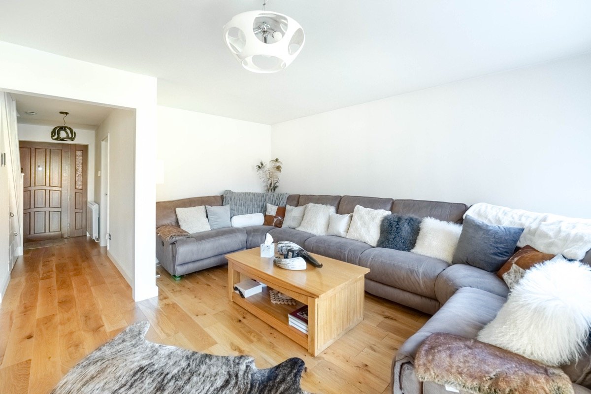 Living room with a grey sectional sofa and oak coffee table, with a view through to the hallway